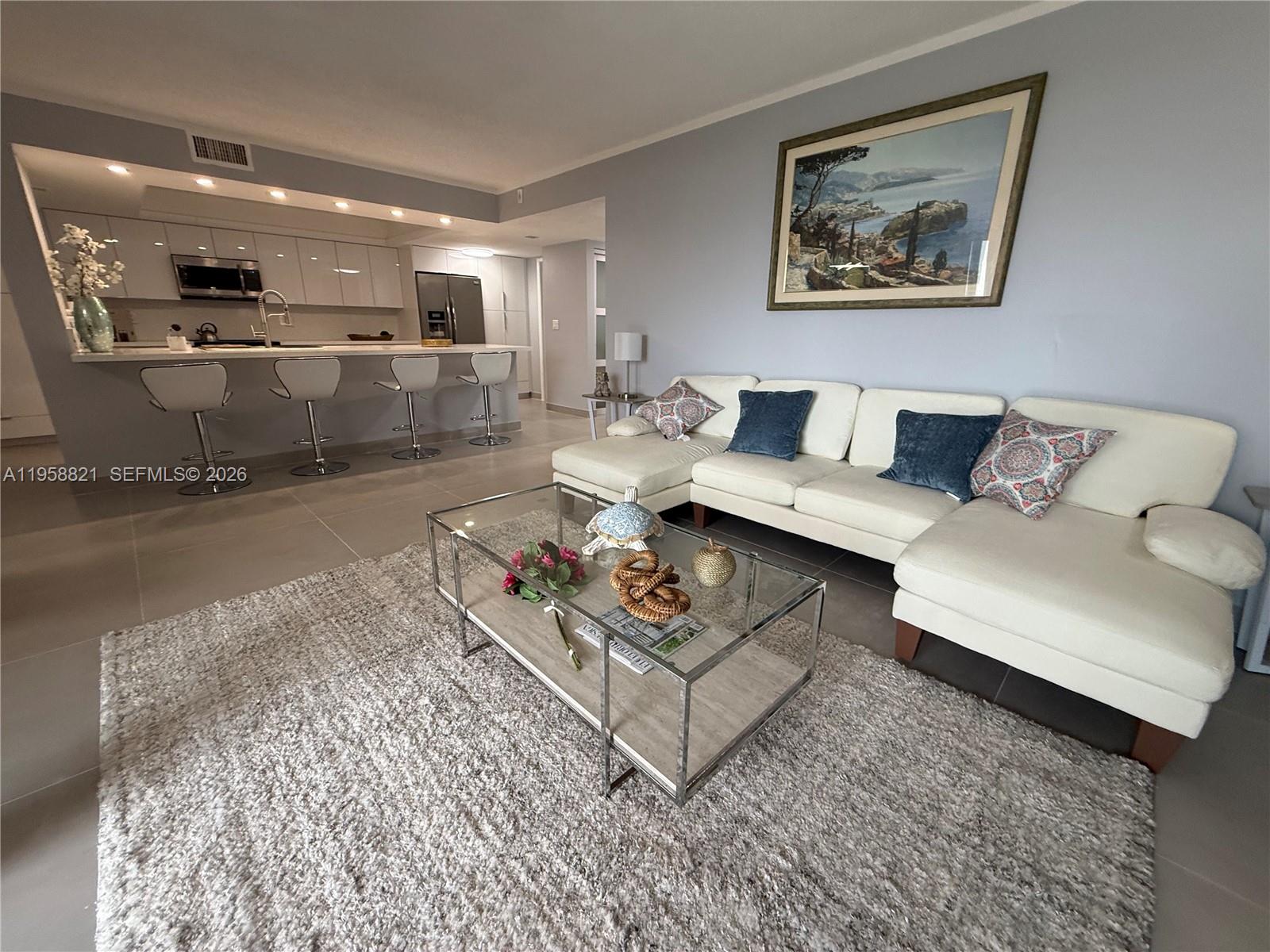 A modern living room features a white sectional sofa, glass coffee table, and open kitchen — 950 Egret Cir # 5409, Delray Beach FL 33444, DELRAY BEACH, FL