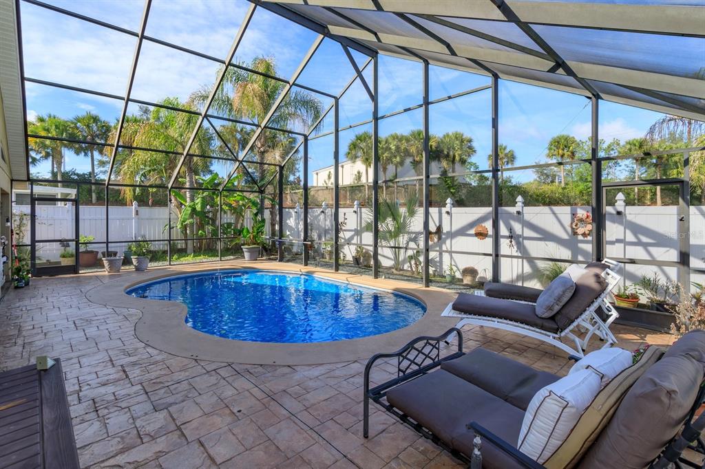 A screened-in patio features a kidney-shaped swimming pool, stone-patterned pavers, and outdoor lounge furniture — 2505 ARRAN CT, CLERMONT, FL
