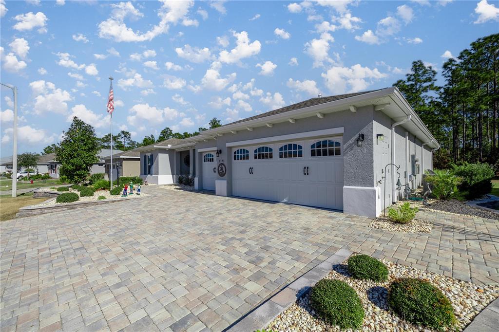 A gray single-story house features a paved driveway, a three-car garage, and landscaped rock beds — 9343 SW 102ND AVENUE ROAD, OCALA, FL