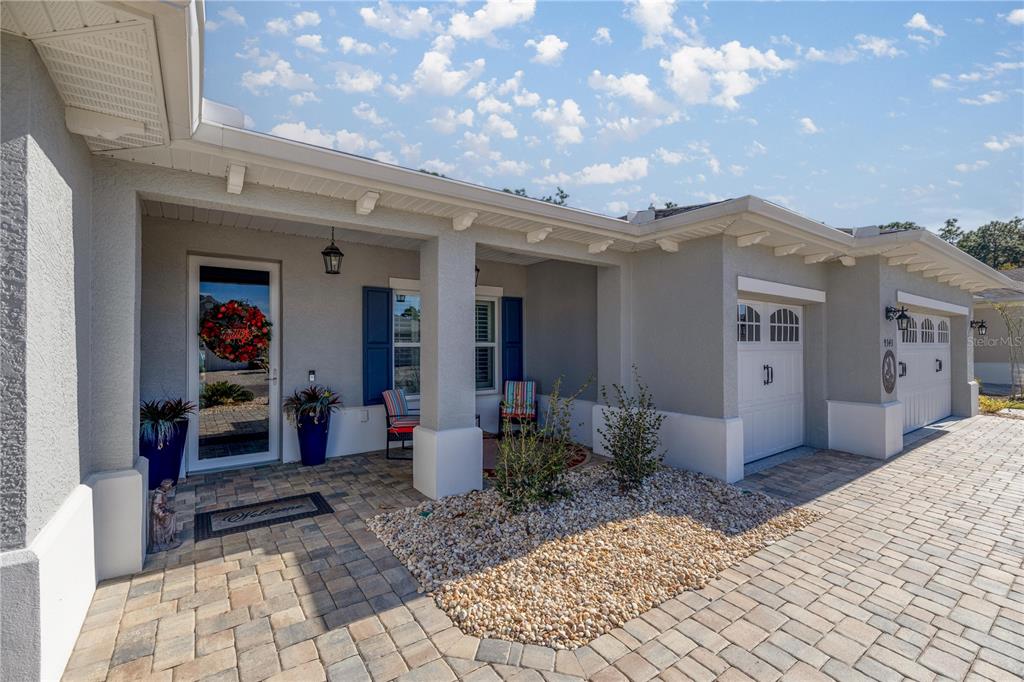 A light-colored house exterior features a paved driveway, a covered porch, and two garage doors — 9343 SW 102ND AVENUE ROAD, OCALA, FL