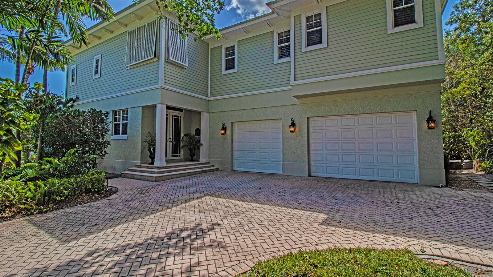 A two-story house with light green siding, a brick paver driveway, and two garage doors — 5592 SE Reef Way, Stuart FL 34997, STUART, FL