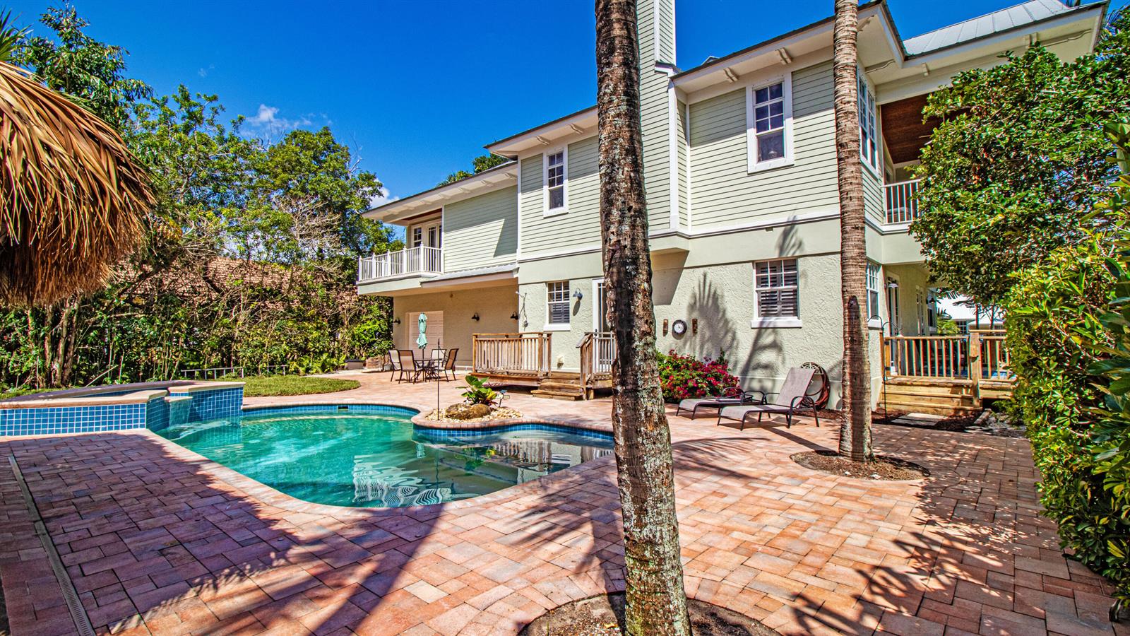 A two-story house with light green siding features a backyard pool and brick patio — 5592 SE Reef Way, Stuart FL 34997, STUART, FL