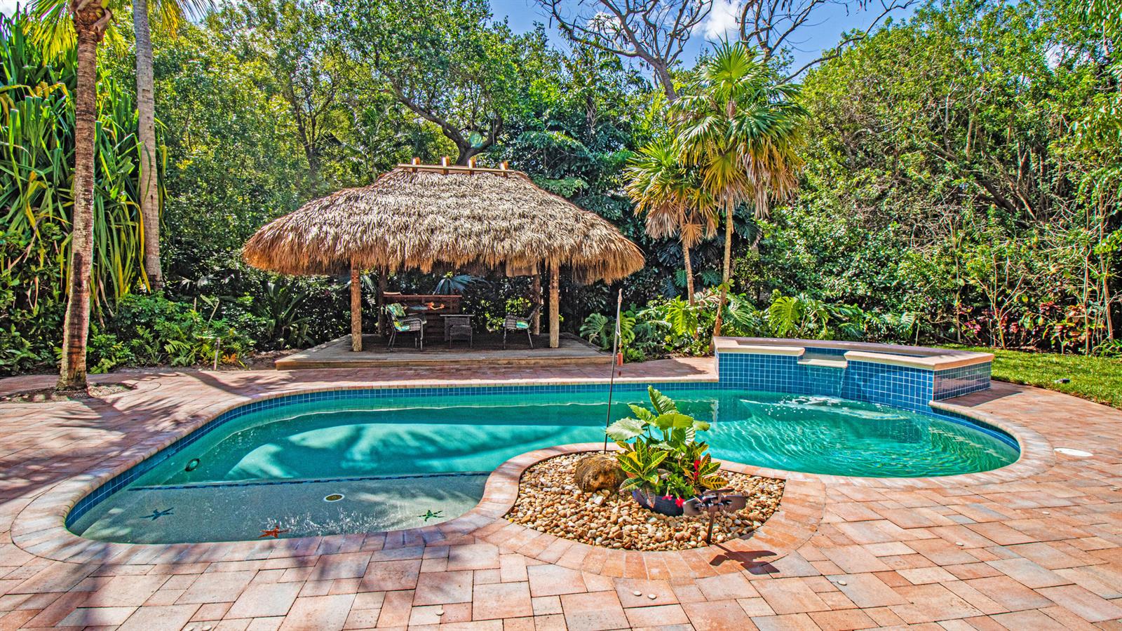 A backyard features a swimming pool with a tiki hut and a stone-paved patio — 5592 SE Reef Way, Stuart FL 34997, STUART, FL