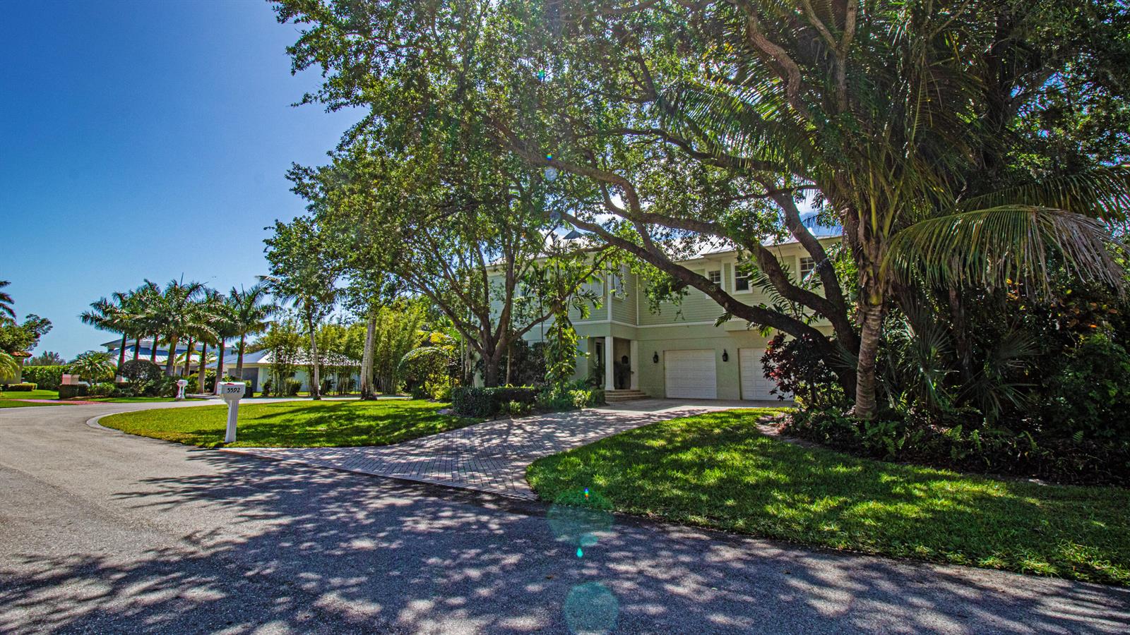 A two-story light green house with a paved driveway sits behind large trees — 5592 SE Reef Way, Stuart FL 34997, STUART, FL