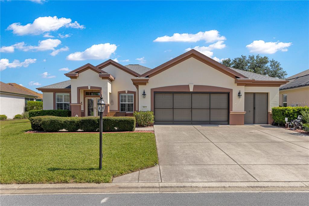 A single-story house with a beige stucco exterior, brown trim, and a three-car garage — 8875 SE 132ND PLACE, SUMMERFIELD, FL