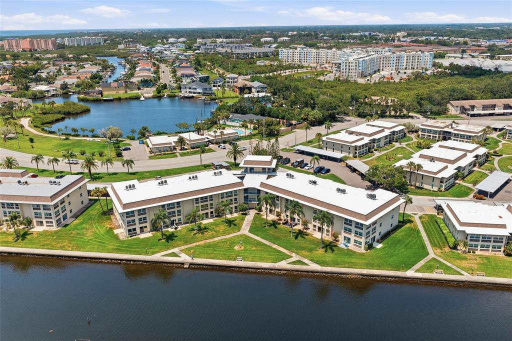 An aerial view shows multi-story apartment buildings situated along a waterfront with green lawns — 4678 MARINE PARKWAY UNIT 105, NEW PORT RICHEY, FL