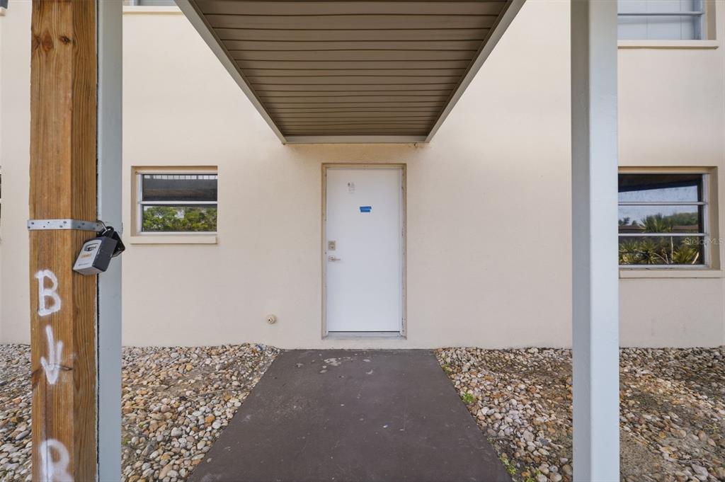 A white exterior door is centered between two windows under a covered walkway — 4678 MARINE PARKWAY UNIT 105, NEW PORT RICHEY, FL