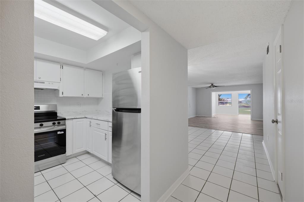 A kitchen with white cabinets and stainless steel appliances opens to a tiled living area — 4678 MARINE PARKWAY UNIT 105, NEW PORT RICHEY, FL