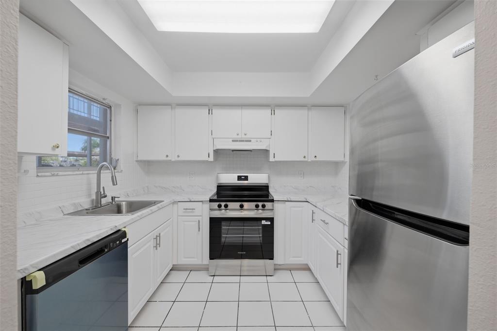 A kitchen with white cabinets, marble-look countertops, stainless steel appliances, and white tile flooring — 4678 MARINE PARKWAY UNIT 105, NEW PORT RICHEY, FL