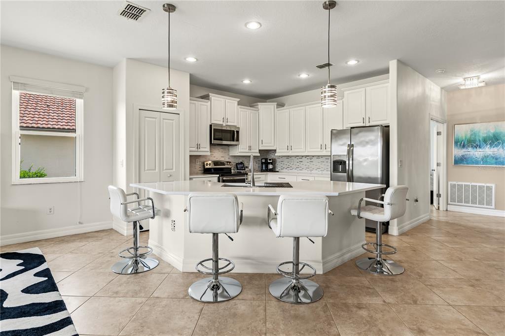 A kitchen features white cabinets, a large central island with bar stools, and tile flooring — 1375 PALMETTO DUNES STREET, DAVENPORT, FL