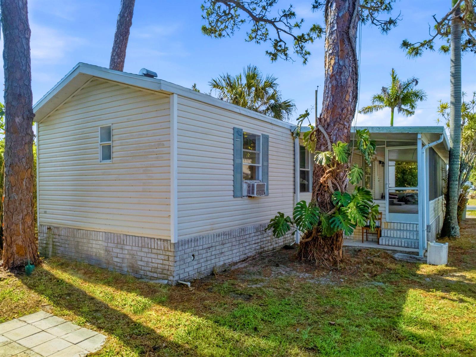 A light-colored mobile home with a brick base sits among trees on a grassy lot — 4185 N Shady Lane, Boynton Beach FL 33436, BOYNTON BEACH, FL