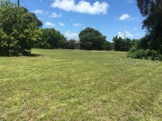 A large, grassy vacant lot is surrounded by mature trees under a blue sky — 106 GULF AVENUE, NOKOMIS, FL