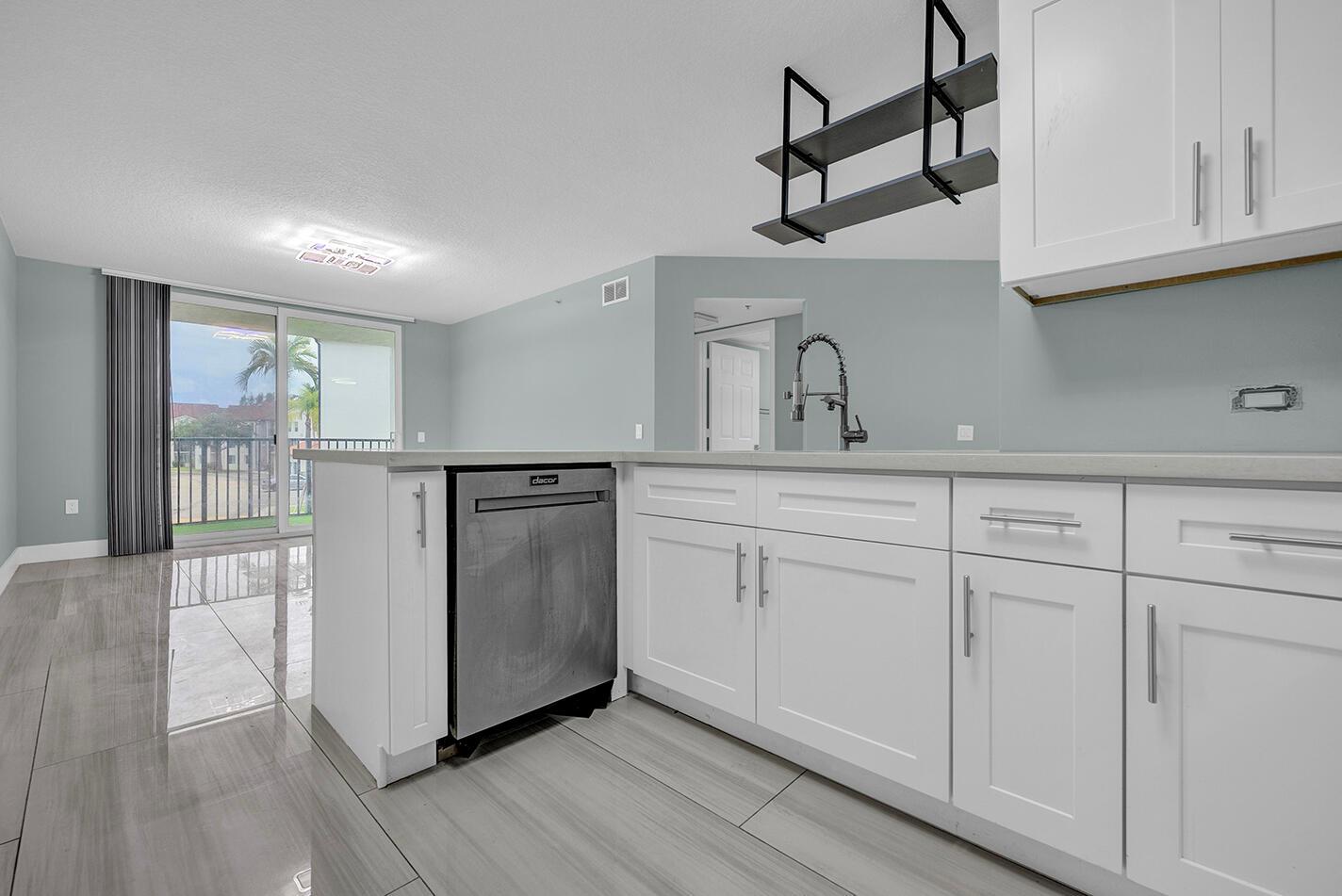 A kitchen with white cabinets, a stainless steel dishwasher, and tile flooring overlooks a balcony — 1010 Villa Circle, Boynton Beach FL 33435, BOYNTON BEACH, FL