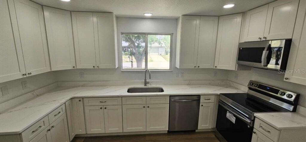 A kitchen features white cabinetry, light-colored countertops, a stainless steel sink, and stainless steel appliances — 10842 SW 90TH COURT, OCALA, FL