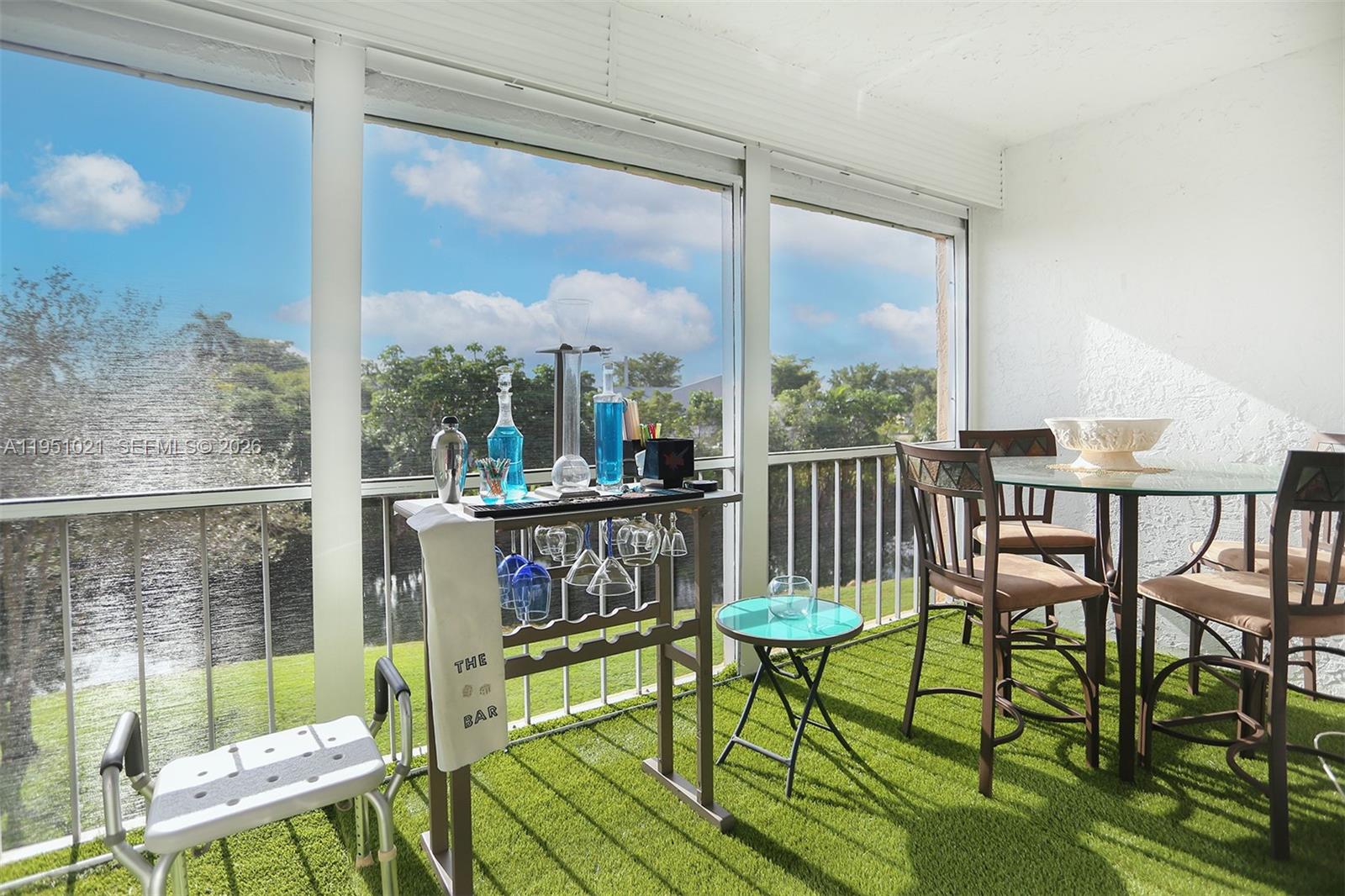 A sunroom with artificial turf flooring, a bar cart, and a dining set overlooks water — 6570 Royal Palm Blvd # 301J, Margate FL 33063, MARGATE, FL