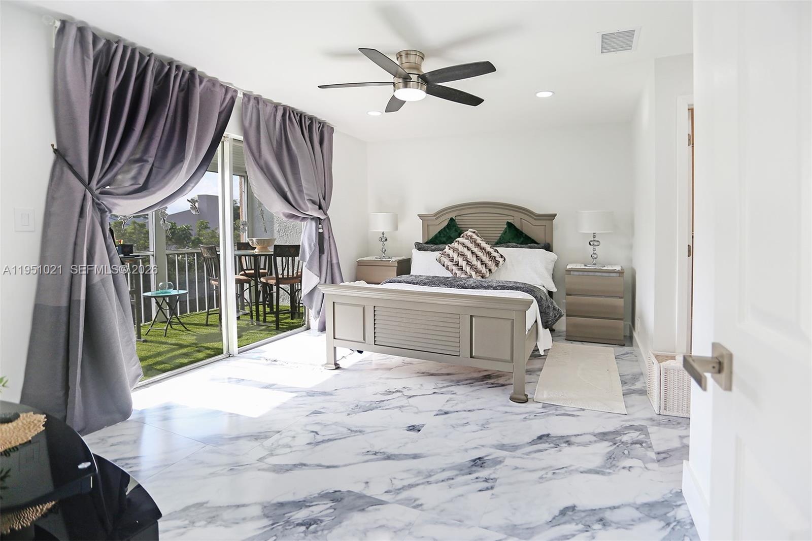 A bedroom features a bed, marble-patterned tile floors, and a sliding door to a balcony — 6570 Royal Palm Blvd # 301J, Margate FL 33063, MARGATE, FL