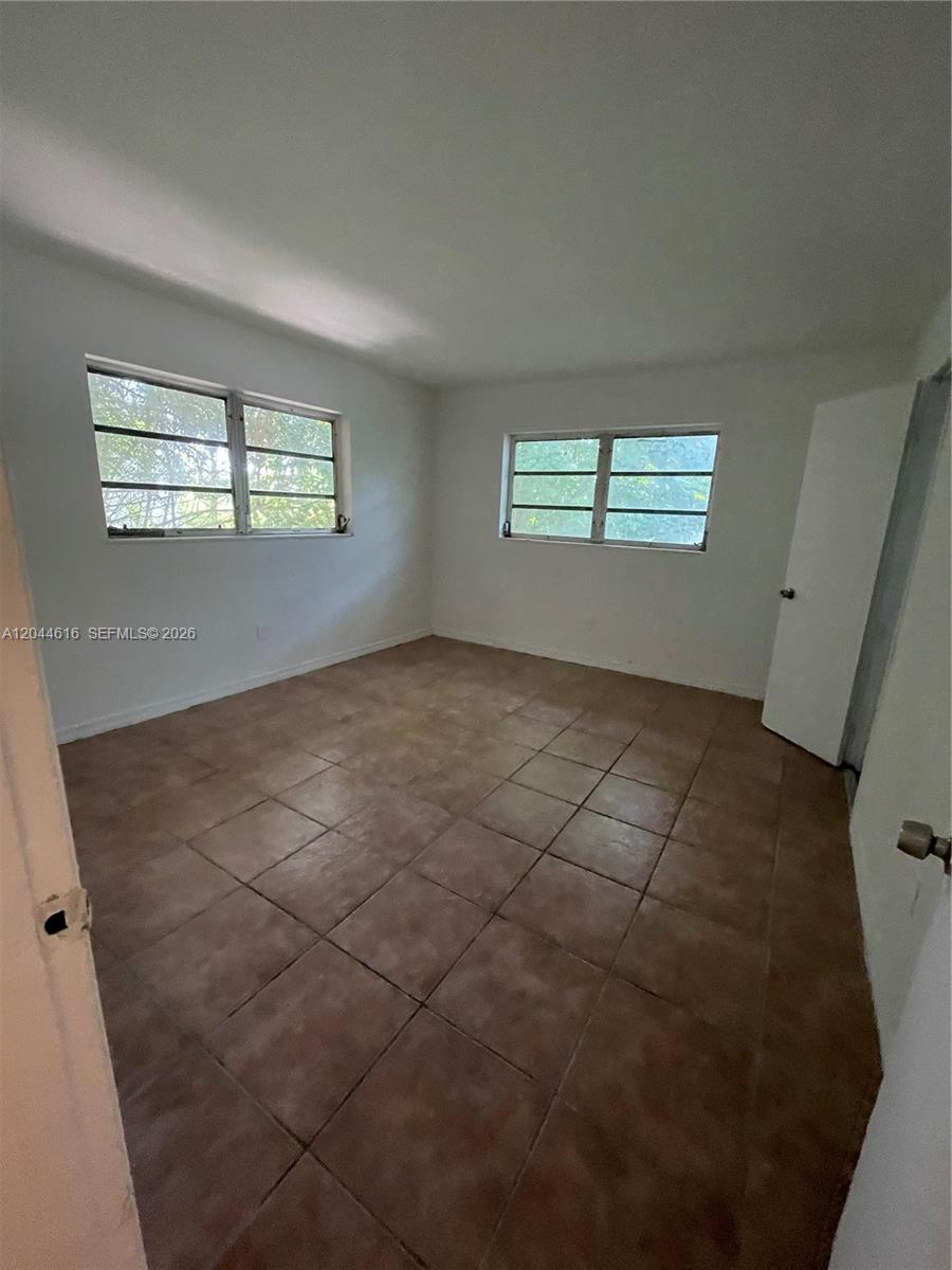 An empty bedroom features white walls, two windows, and brown tile flooring — 7841 Dunham Blvd # 6, Miami FL 33138, MIAMI, FL