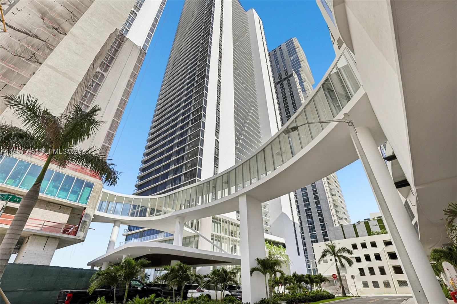 A low-angle exterior view shows a modern high-rise building connected by a glass-enclosed pedestrian bridge — 700 NE 24th St # 806, Miami FL 33137, MIAMI, FL