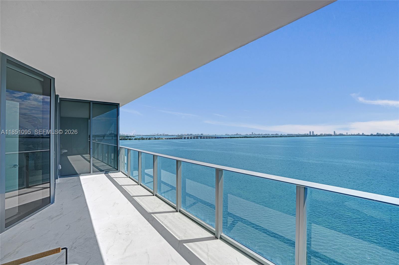 A balcony with glass railings overlooks a large body of water and a distant bridge — 700 NE 24th St # 806, Miami FL 33137, MIAMI, FL