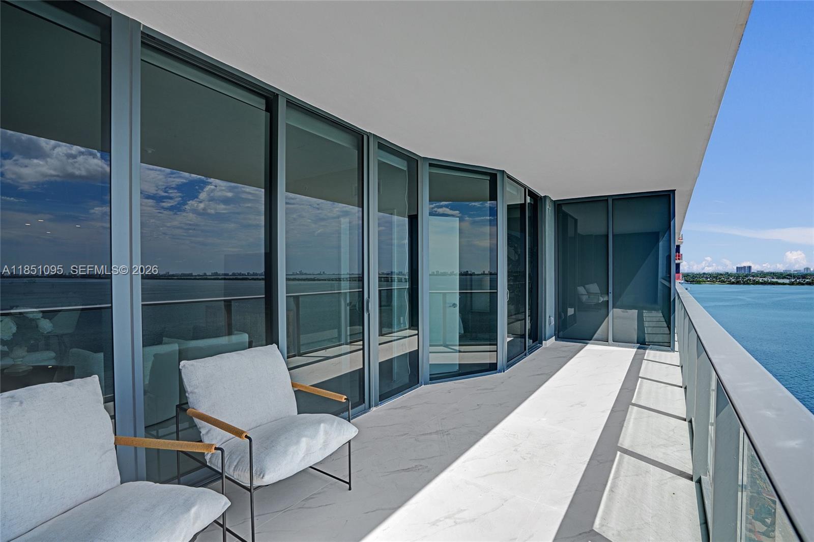 A balcony with white marble flooring, glass railings, and two chairs overlooking the water — 700 NE 24th St # 806, Miami FL 33137, MIAMI, FL