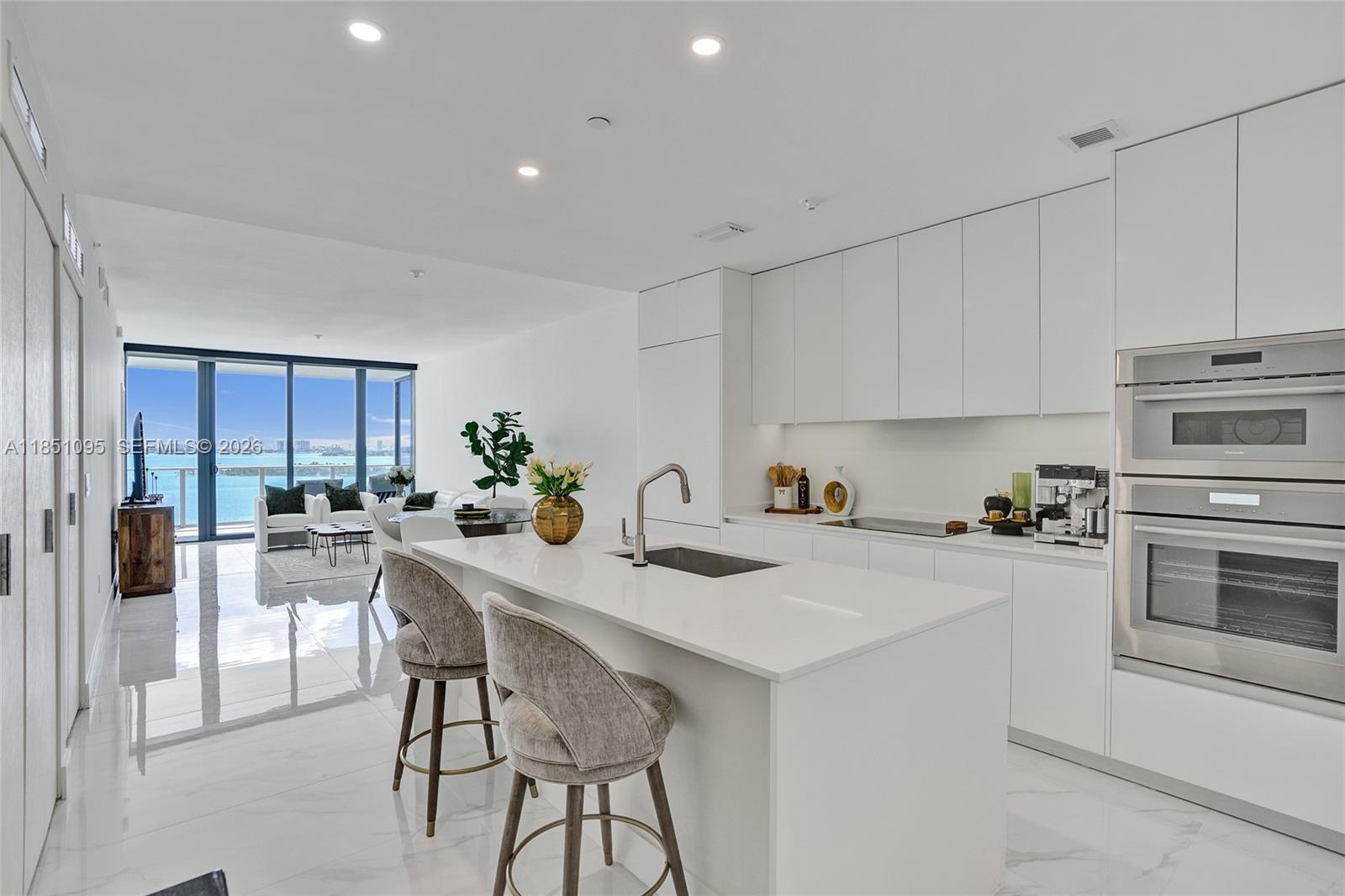 A modern white kitchen features a central island with bar stools and a water view — 700 NE 24th St # 806, Miami FL 33137, MIAMI, FL
