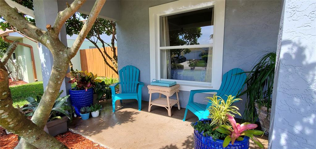 A covered porch features two bright blue Adirondack chairs, a small wicker table, and potted plants — 4439 Katy DRIVE, NEW SMYRNA BEACH, FL