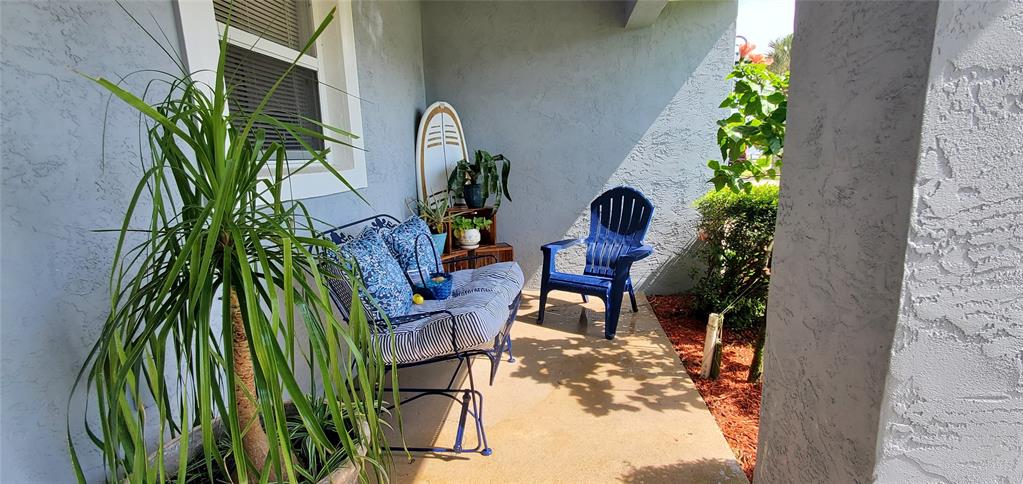 A covered patio features a blue chair, a bench with patterned cushions, and potted plants — 4439 Katy DRIVE, NEW SMYRNA BEACH, FL