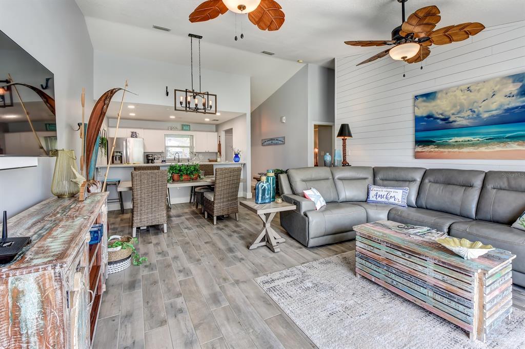 An open-concept living and dining area features gray wood-look tile flooring and coastal decor — 4439 Katy DRIVE, NEW SMYRNA BEACH, FL
