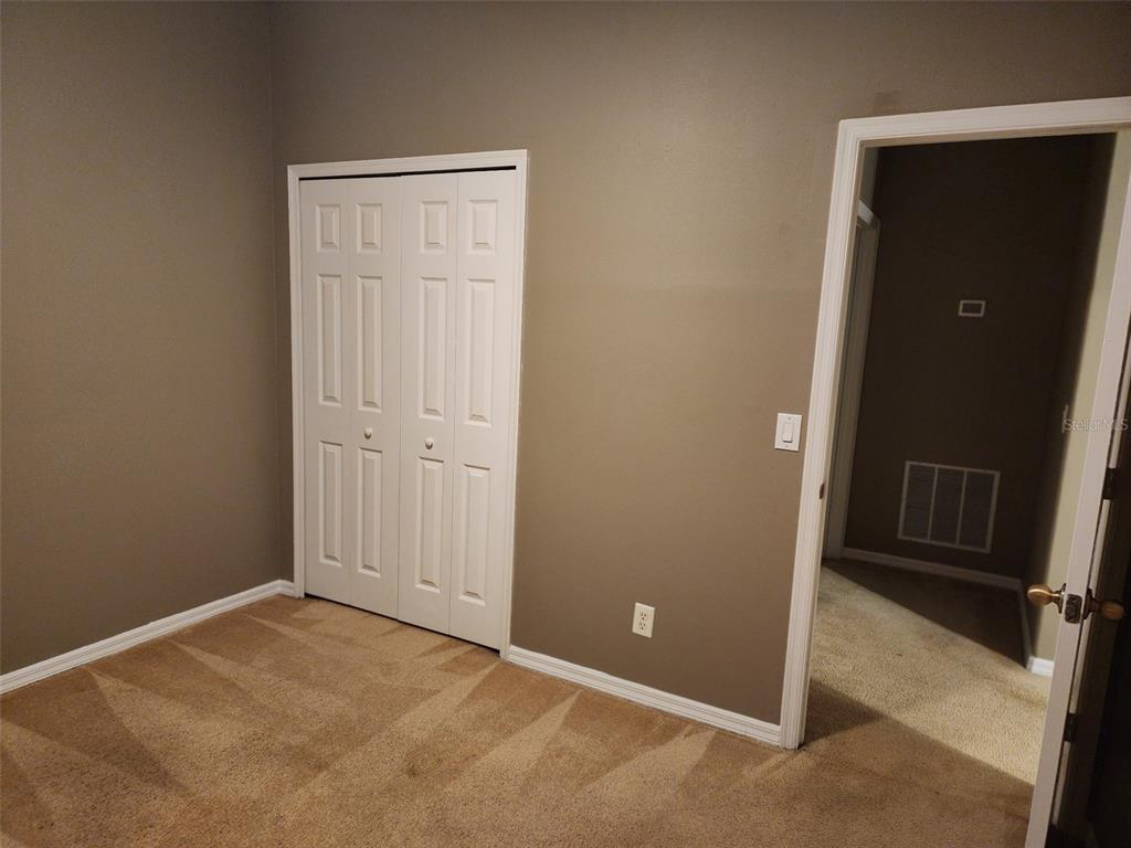 A bedroom with beige carpet, taupe walls, a white bifold closet door, and an open doorway — 4025 SHAWN CIRCLE, ORLANDO, FL