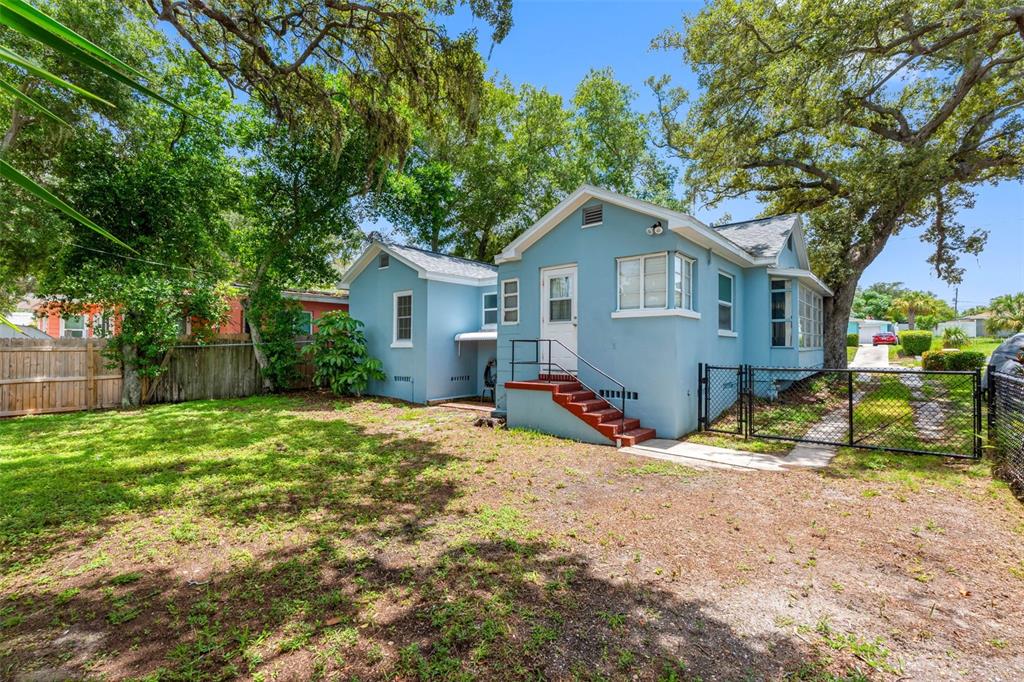 A blue house with a red-stepped back entrance sits in a grassy, tree-shaded yard — 1010 OSAGE STREET, CLEARWATER, FL