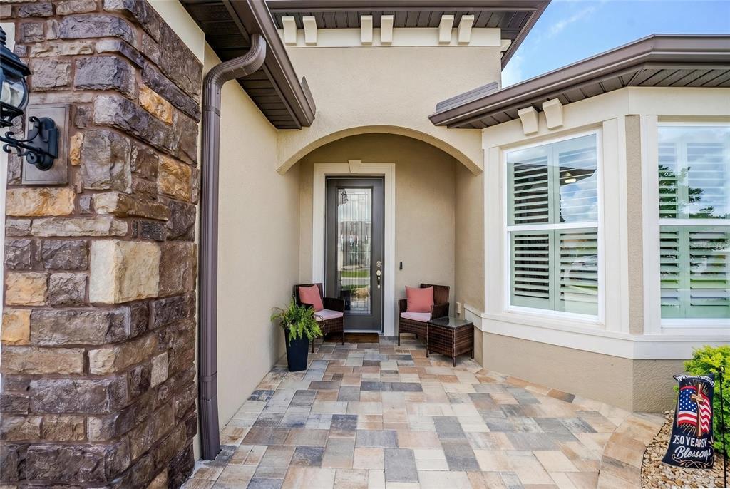 A stone-accented home entrance features a paved porch, a glass-paneled front door, and two chairs — 6038 SW 86TH CIRCLE, OCALA, FL