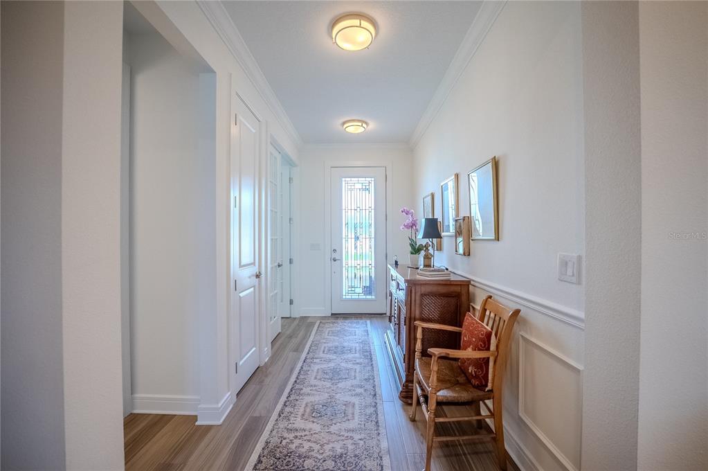 A bright entryway features wood-look flooring, white wainscoting, a wooden console table, and a runner rug — 6038 SW 86TH CIRCLE, OCALA, FL