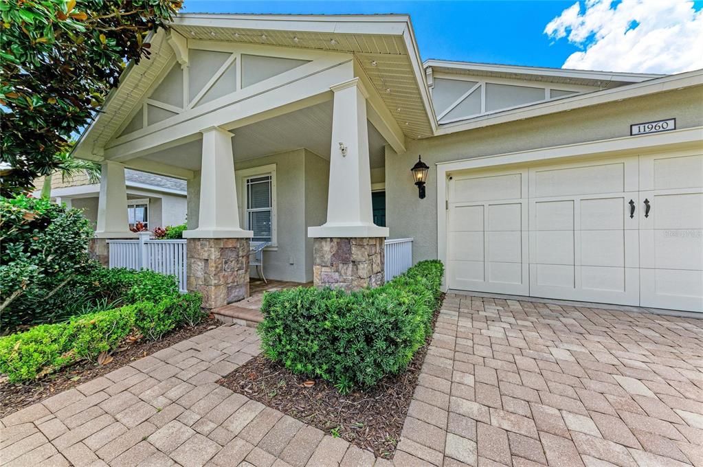 The exterior of a house features a stone-based porch, a white garage door, and landscaping — 11960 FOREST PARK CIRCLE, BRADENTON, FL
