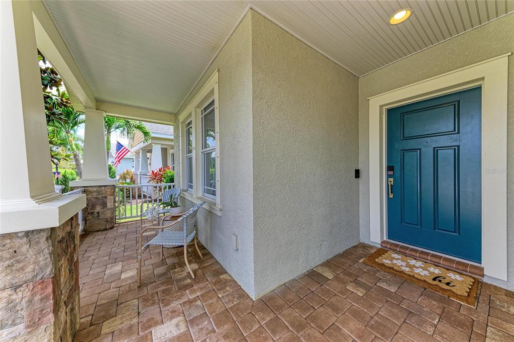 A covered front porch features stone-based columns, paver flooring, and a blue front door — 11960 FOREST PARK CIRCLE, BRADENTON, FL