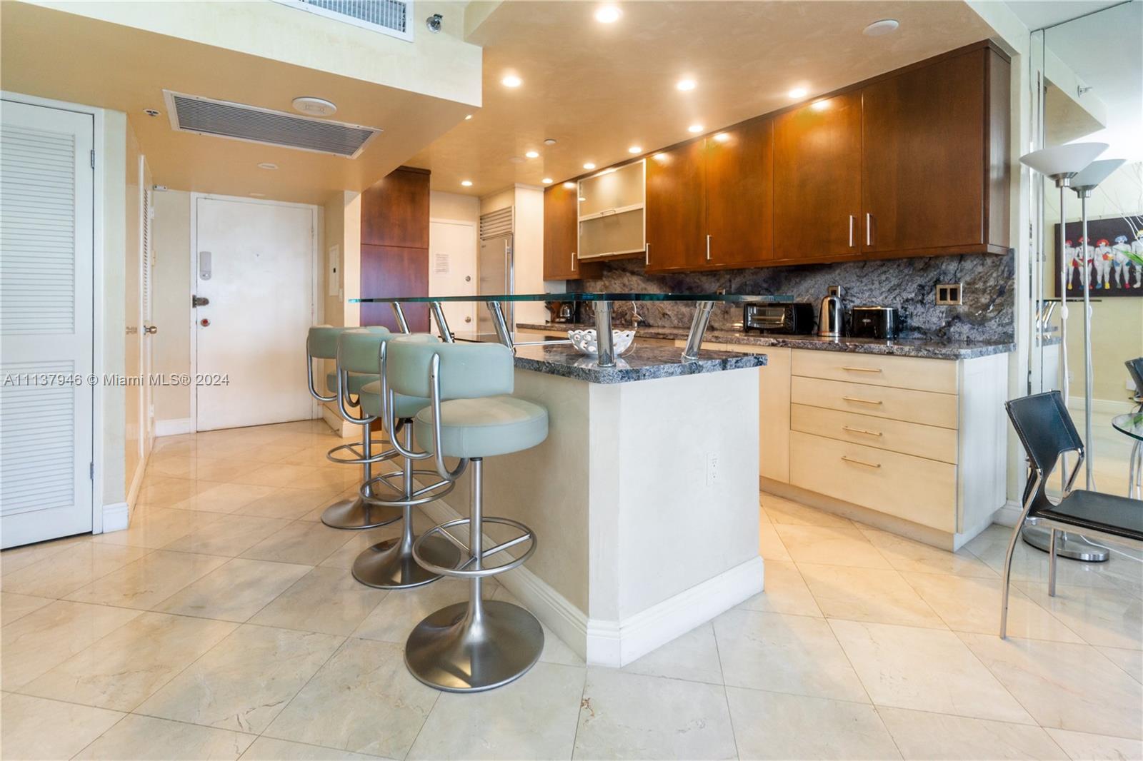 A kitchen features a glass-topped breakfast bar, light-colored cabinetry, and dark wood upper cabinets — 100 Lincoln Rd # 1533, Miami Beach FL 33139, MIAMI BEACH, FL