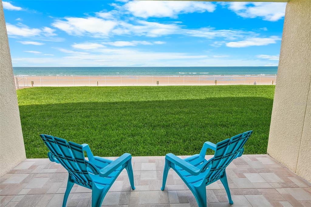 Two blue chairs sit on a paved patio overlooking a grassy lawn and the ocean — 4495 S ATLANTIC AVENUE UNIT 104, PONCE INLET, FL