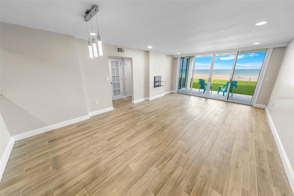 An empty room with wood-look tile flooring, a modern light fixture, and sliding glass doors — 4495 S ATLANTIC AVENUE UNIT 104, PONCE INLET, FL