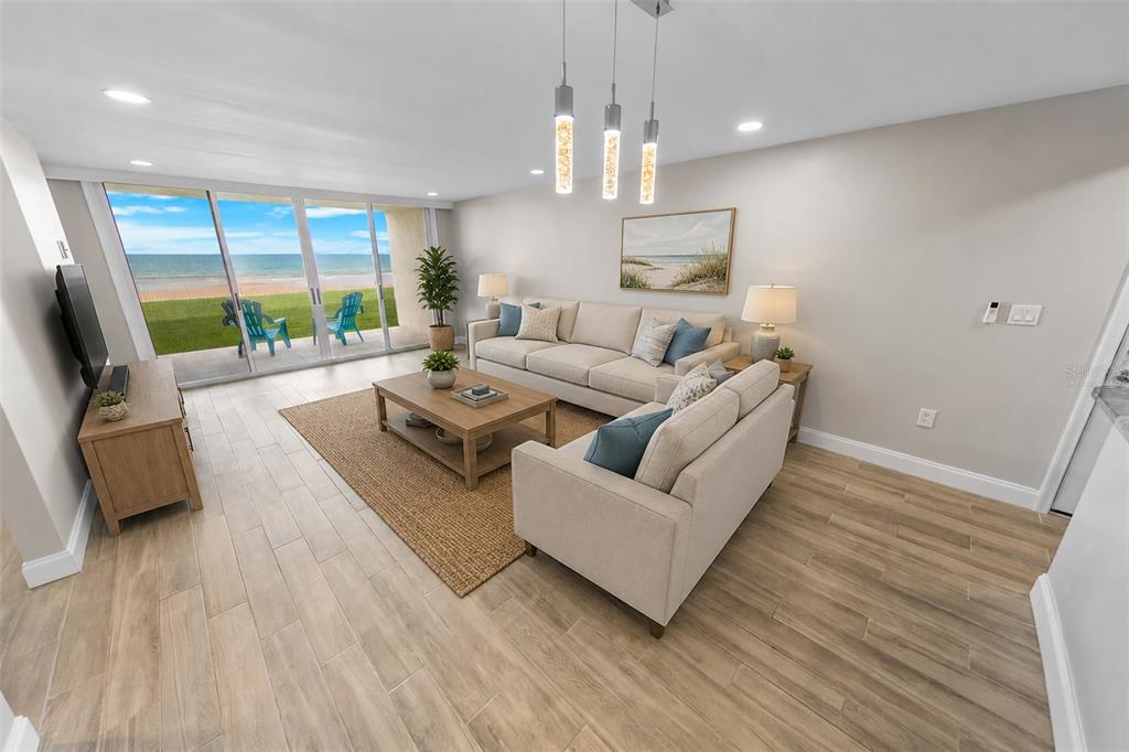 A living room with light wood-look tile floors, beige sofas, and sliding doors overlooking the ocean — 4495 S ATLANTIC AVENUE UNIT 104, PONCE INLET, FL