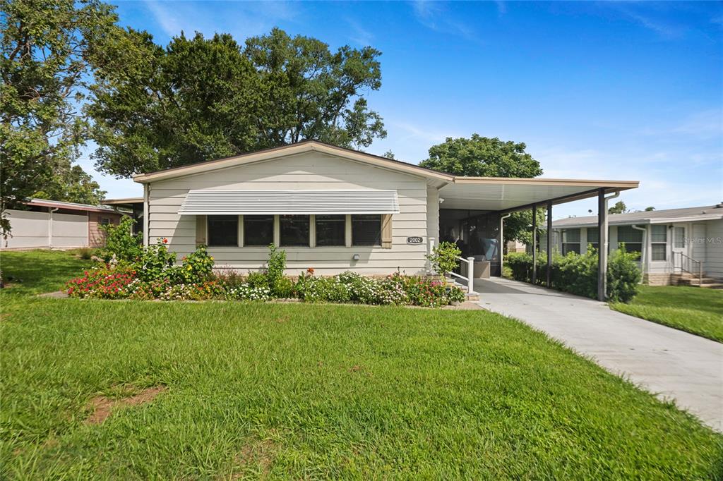 A single-story house with light siding, a front garden, and an attached carport — 2002 S CITRUS CIRCLE UNIT 1728, ZELLWOOD, FL