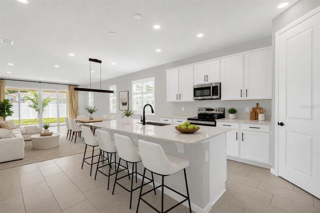 A modern open-concept kitchen features white cabinetry, a quartz island with bar seating, and tile flooring — 3998 BANNOCK AVENUE, TAVARES, FL