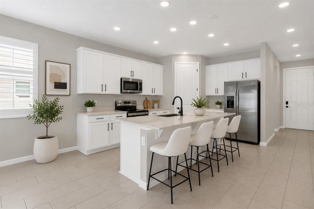 A modern kitchen features white cabinetry, stainless steel appliances, a quartz island, and tile flooring — 3998 BANNOCK AVENUE, TAVARES, FL