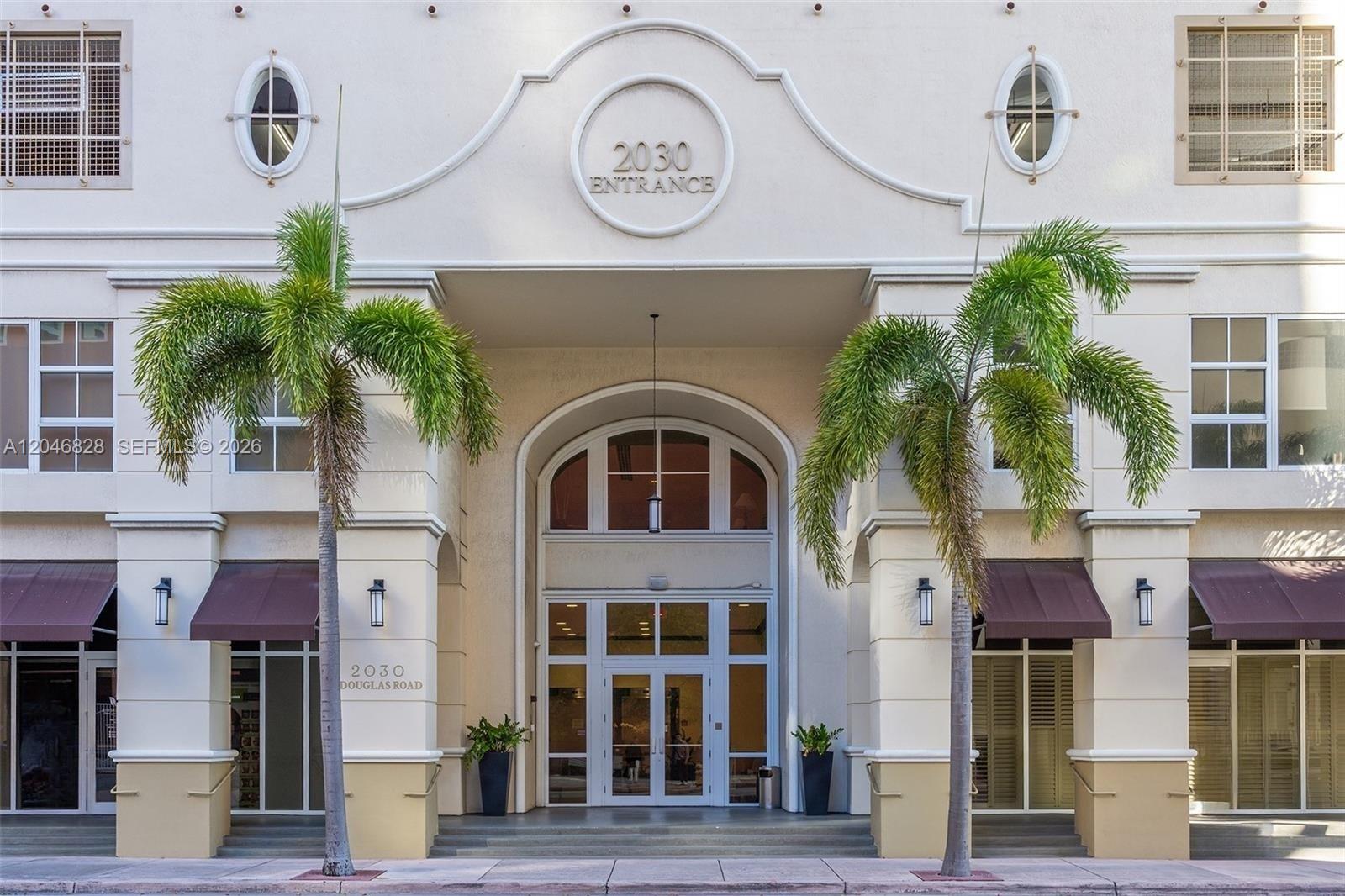 The exterior of a multi-story building features a central arched entrance flanked by two palm trees — 2030 S Douglas Rd # 716, Coral Gables FL 33134, CORAL GABLES, FL
