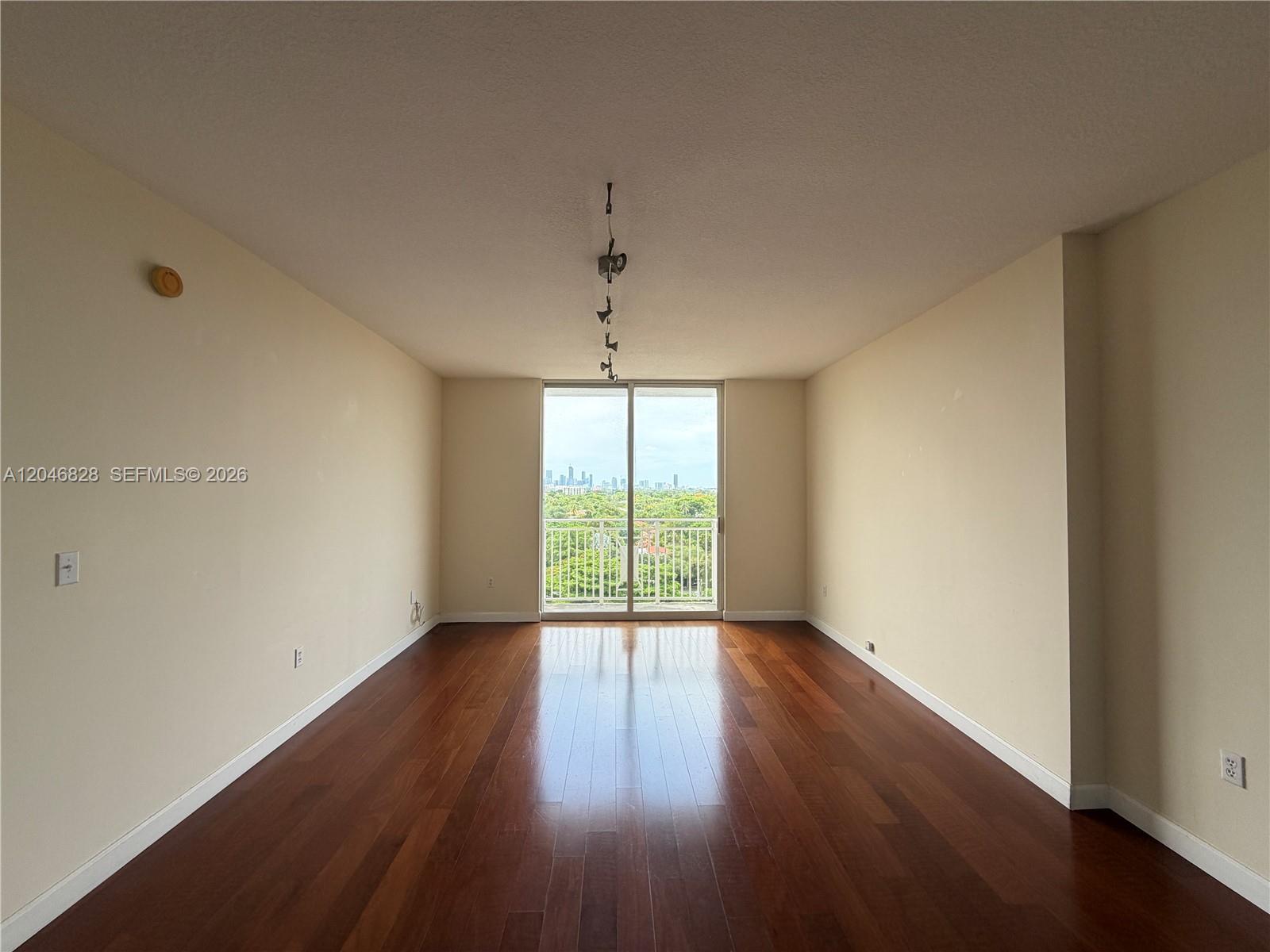 An empty room features dark hardwood floors, beige walls, and a balcony with city views — 2030 S Douglas Rd # 716, Coral Gables FL 33134, CORAL GABLES, FL