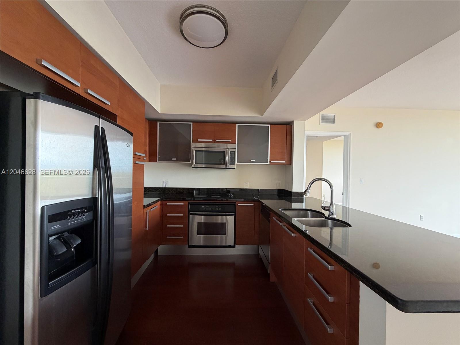 A kitchen features wood cabinets, stainless steel appliances, and a black granite countertop — 2030 S Douglas Rd # 716, Coral Gables FL 33134, CORAL GABLES, FL