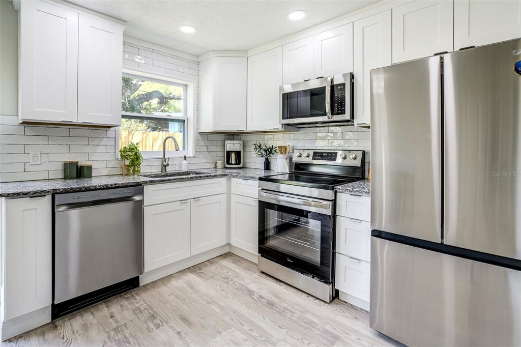 A kitchen features white cabinets, stainless steel appliances, granite countertops, and a subway tile backsplash — 3579 POCAHONTAS DRIVE, LARGO, FL