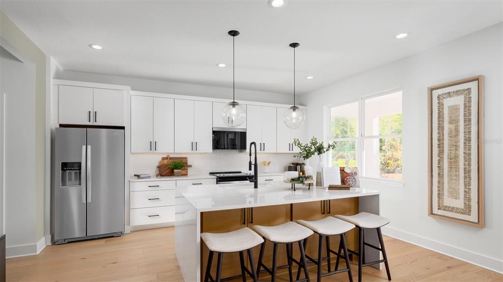 A modern kitchen features white cabinetry, a wood-toned island with bar seating, and stainless appliances — 8031 TIMBERWOOD LANE, ORLANDO, FL
