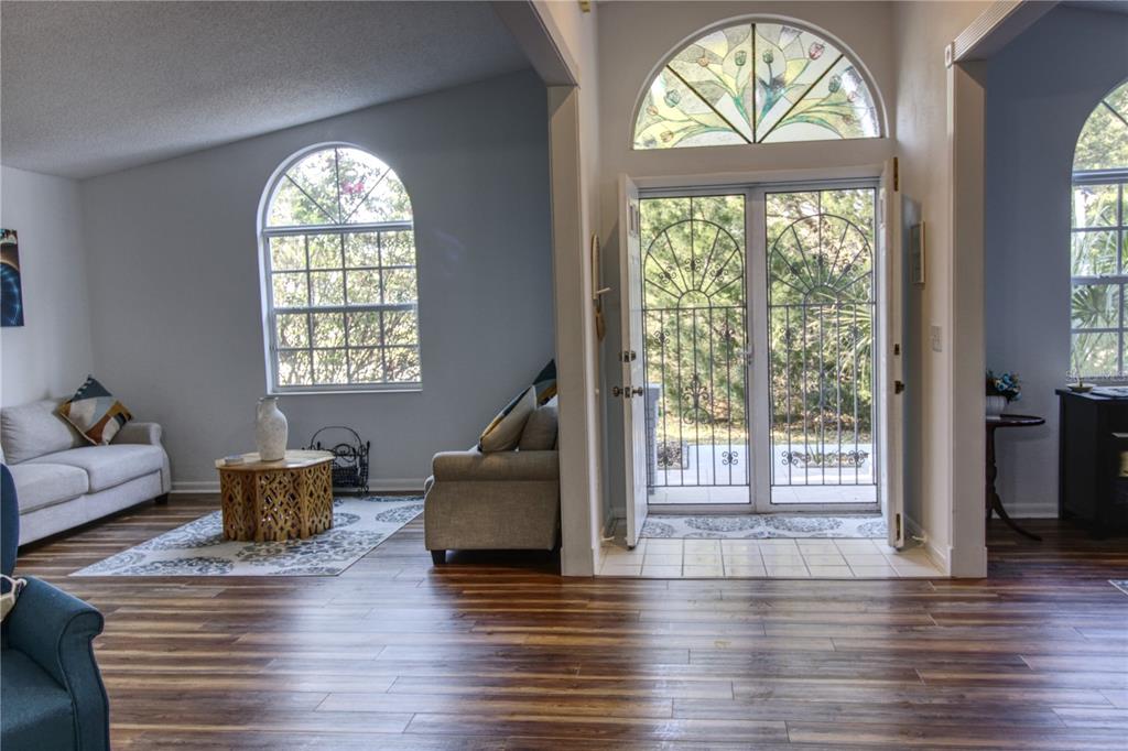 A living room features wood-look flooring, a stained-glass arched window, and double glass entry doors — 2 SEAGIRT COURT, PALM COAST, FL