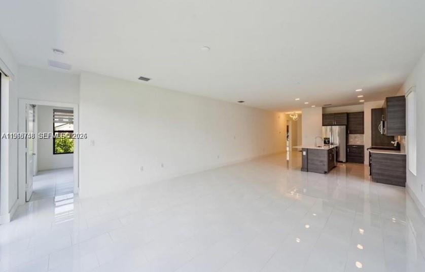 An open-concept living area features white tile floors, a kitchen with dark cabinetry, and a doorway — 5501 Agostino way, Ave Maria FL 34142, AVE MARIA, FL