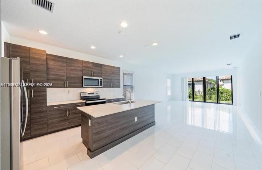 A modern kitchen features dark wood cabinets, a central island, and white tile flooring — 5501 Agostino way, Ave Maria FL 34142, AVE MARIA, FL