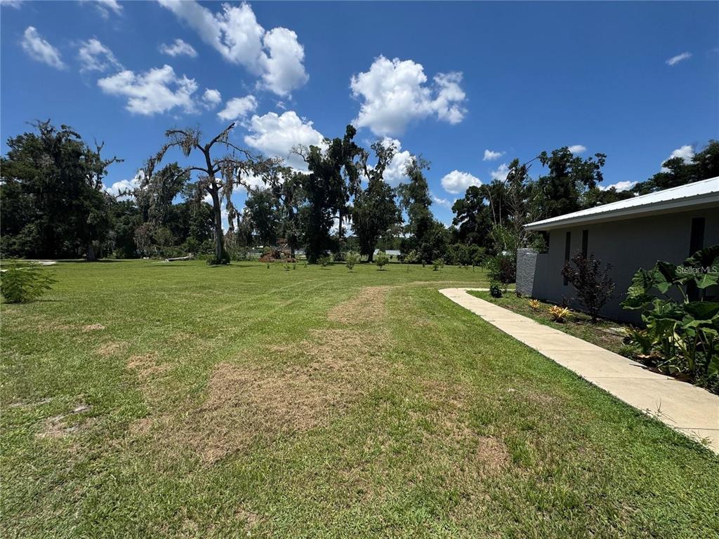 A wide, grassy yard extends from a concrete walkway alongside a gray house exterior — 4925 N US HIGHWAY 441, OCALA, FL